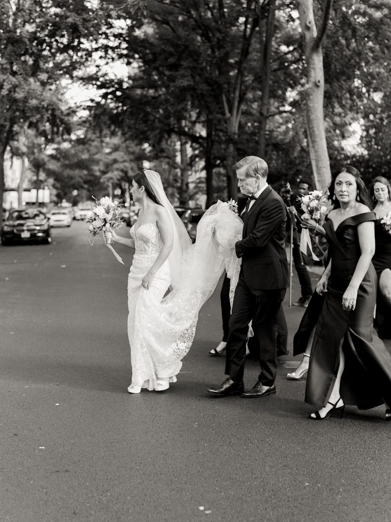 Bride crossing the street with her parents carrying the train of her dress.