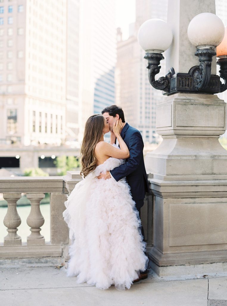 Man and woman kissing against stone pillar with Chicago buildings in the background.