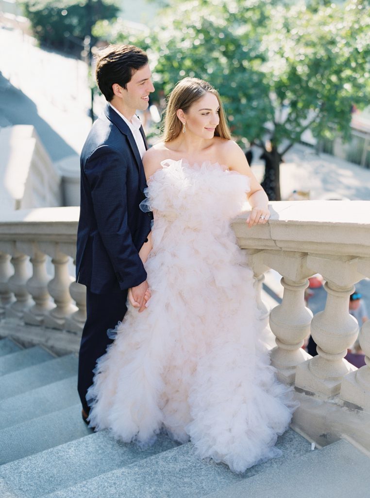 Woman in full length designer gown, and man in suit standing on stone steps for their Chicago engagement session.