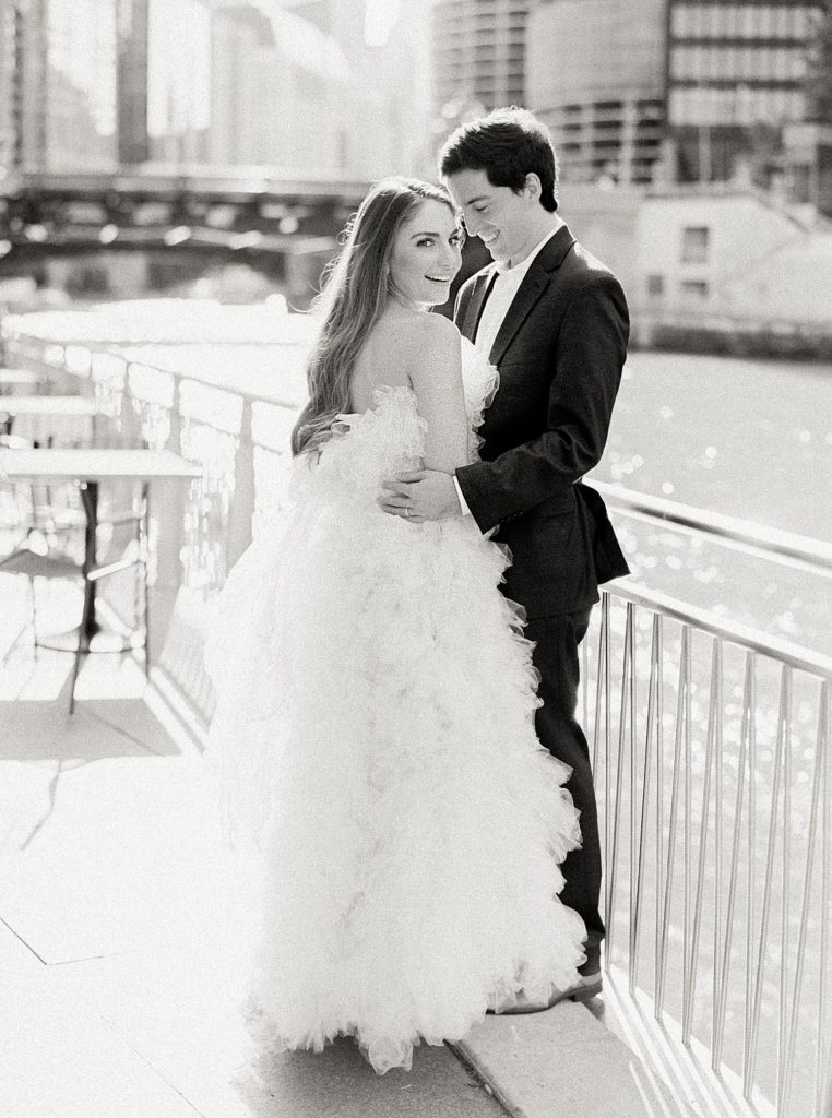 Black and white image of man and woman curled up against a railing on the water, wearing designer clothes.