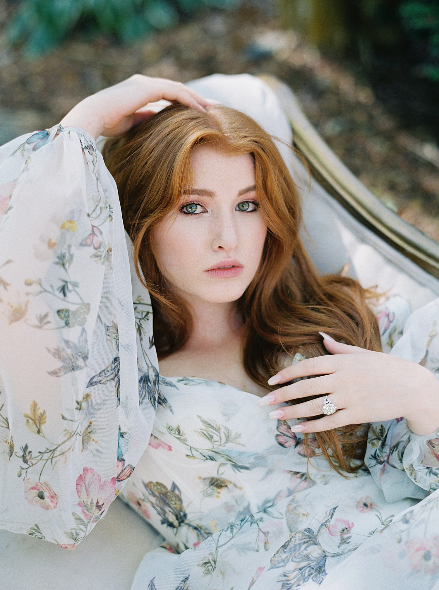 Redhead woman lying on a couch in a floral bodice and gown looking up into the camera.
