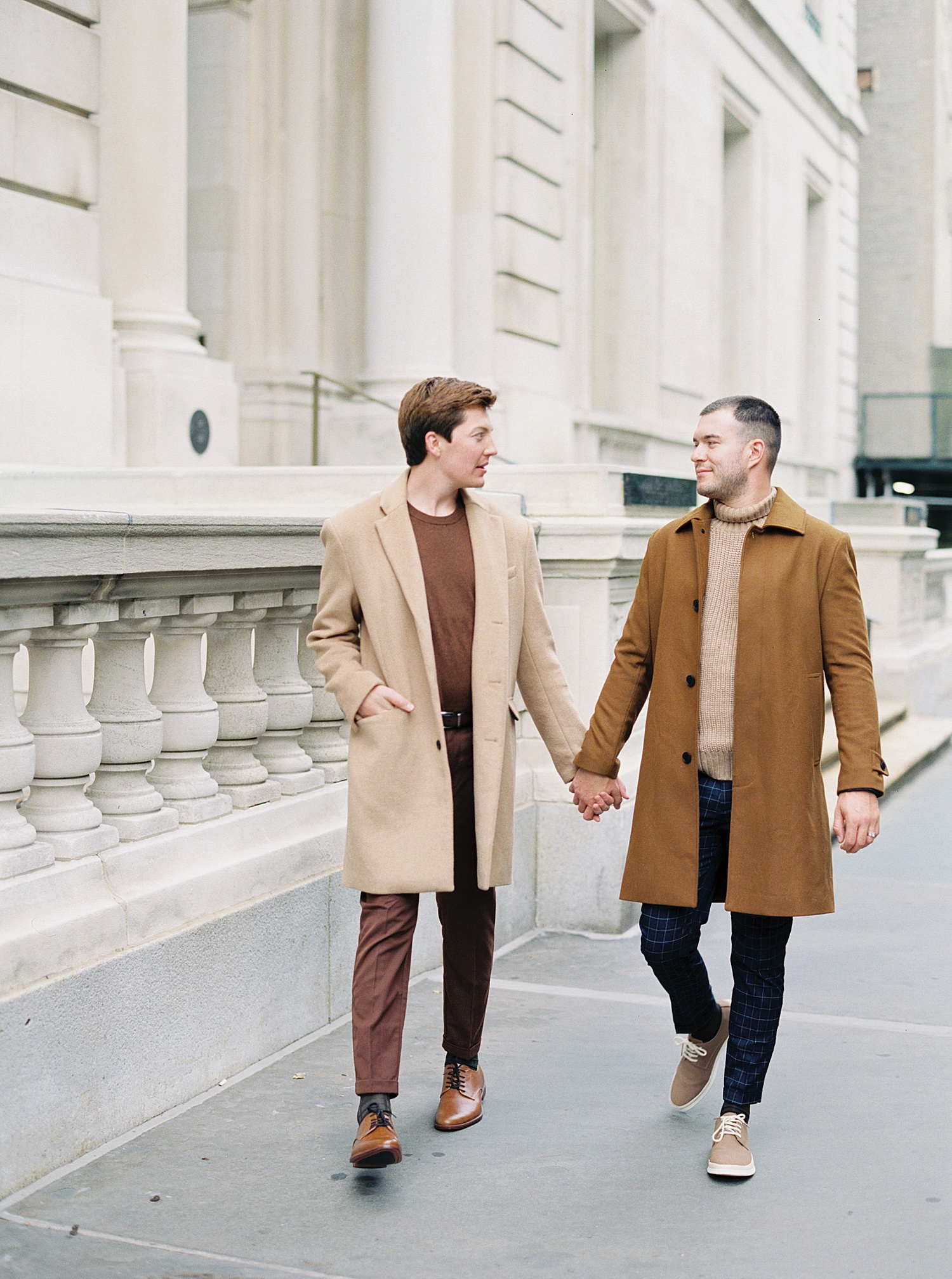 Two men in brown coats, holding hands and walking down the streets of New York.