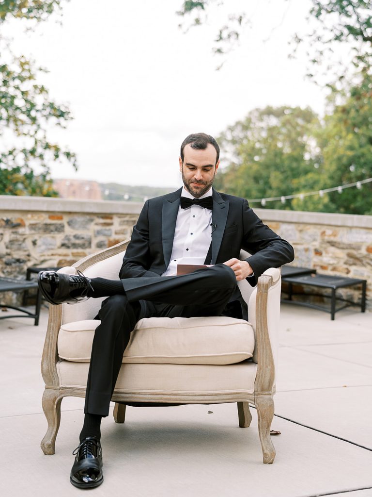 Groom sitting on a patio in a chair waiting for his bride.