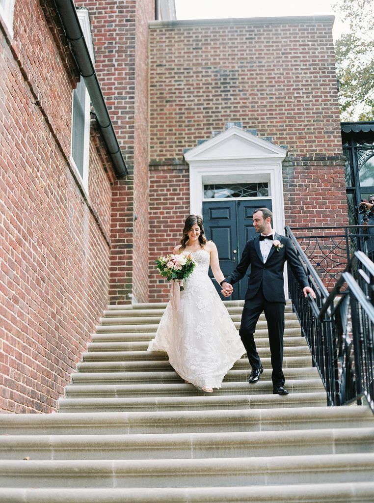 Bride and groom walking down big steps at an old building.