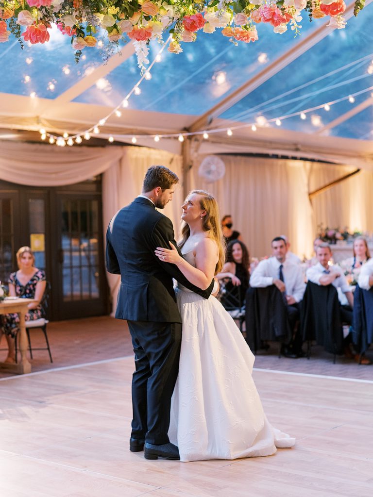 Newlyweds share a first dance at their reception under clear tent.