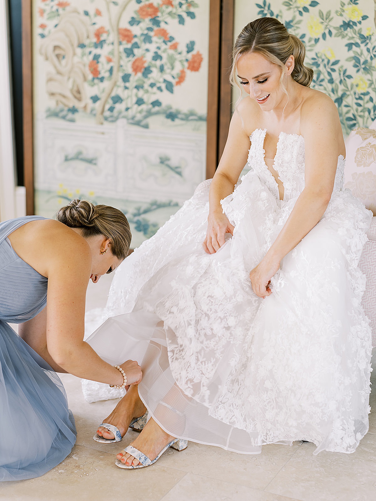 Bridesmaid adjusts bride's floral blue high heel shoe as bridal party gets ready for Chicago summer backyard wedding