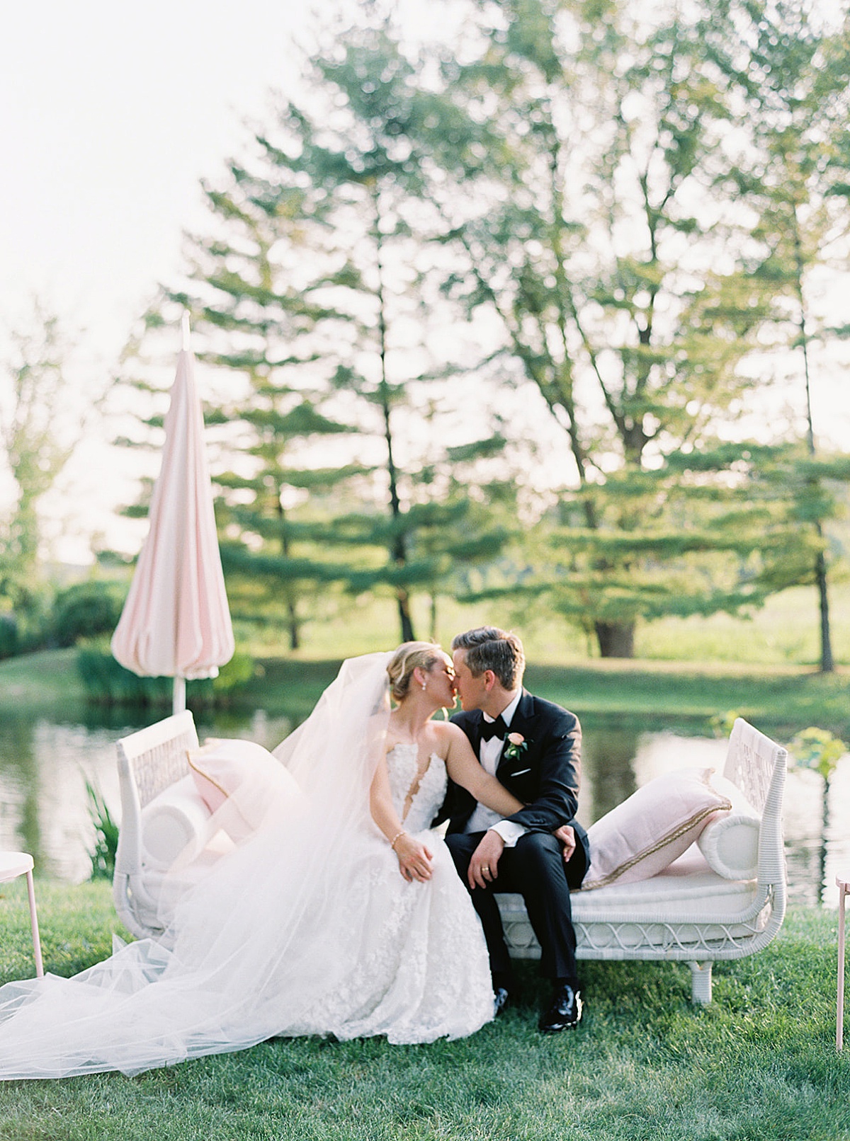 bride and groom share a romantic kiss on chaise lounge in front of pond at chicago wedding shot by destination luxury photographer