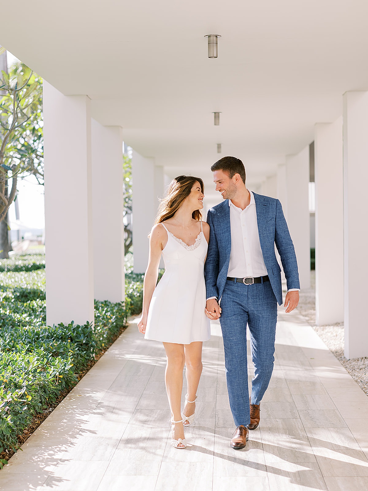 bride in chic minidress and groom in blue linen suit walk through beachside hotel during Anguilla Elopement 
