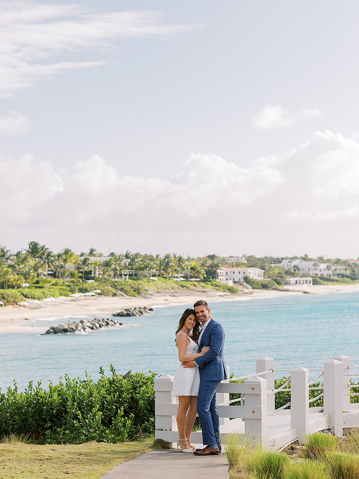 bride in chic minidress and groom in linen suit pose in front of tropical beach during Anguilla Elopement 