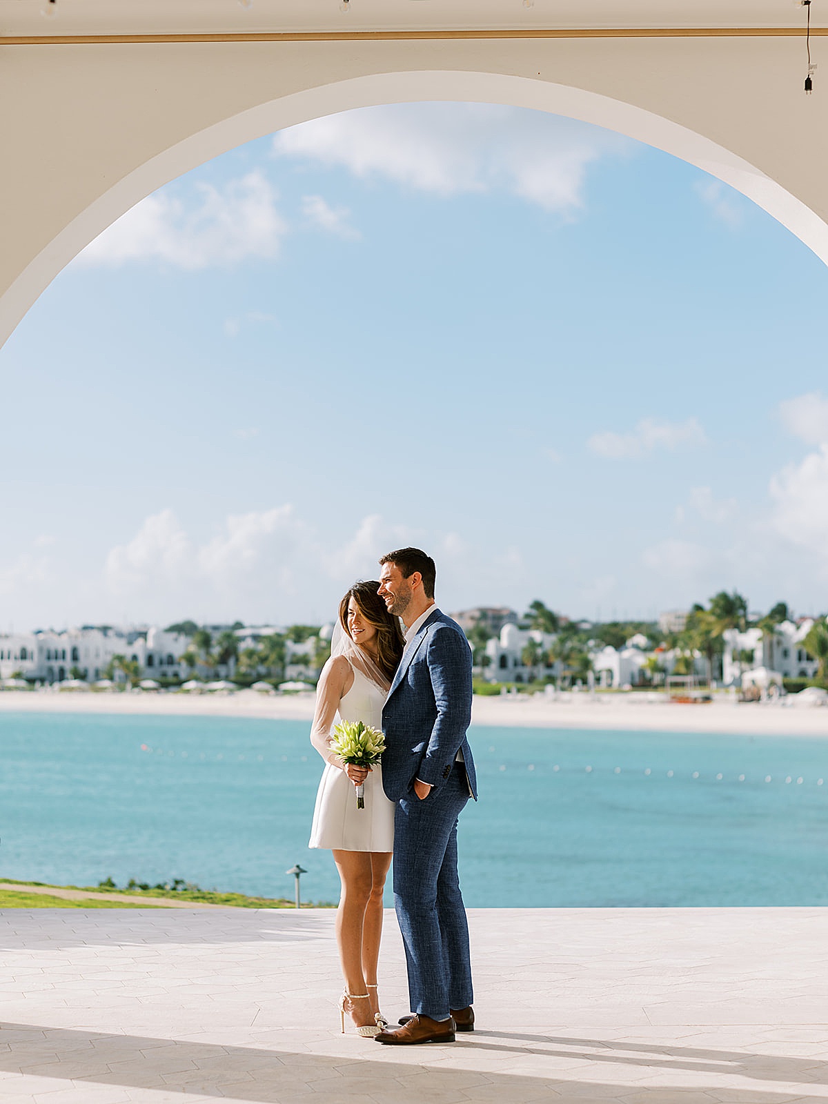 bride in pearl-covered heels and satin minidress poses with groom in beachfront hotel during Anguilla Elopement 