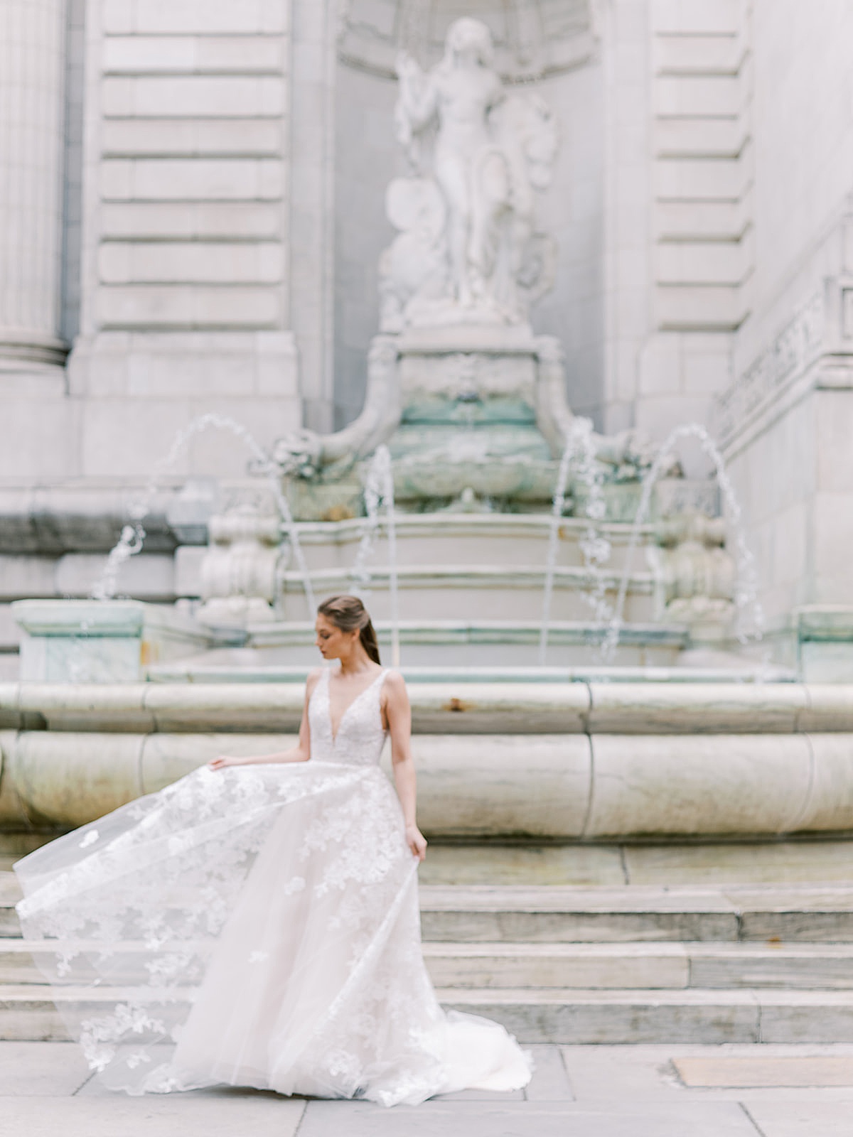 model in modern lace wedding gown poses in front of iconic fountain during shoot with NYC Fashion Photographer